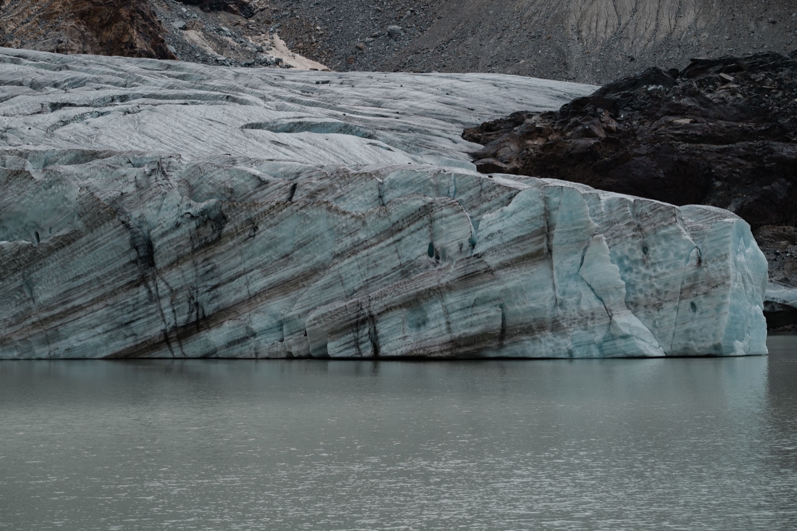 Layered blue-grey glacier ice meeting a quiet lake