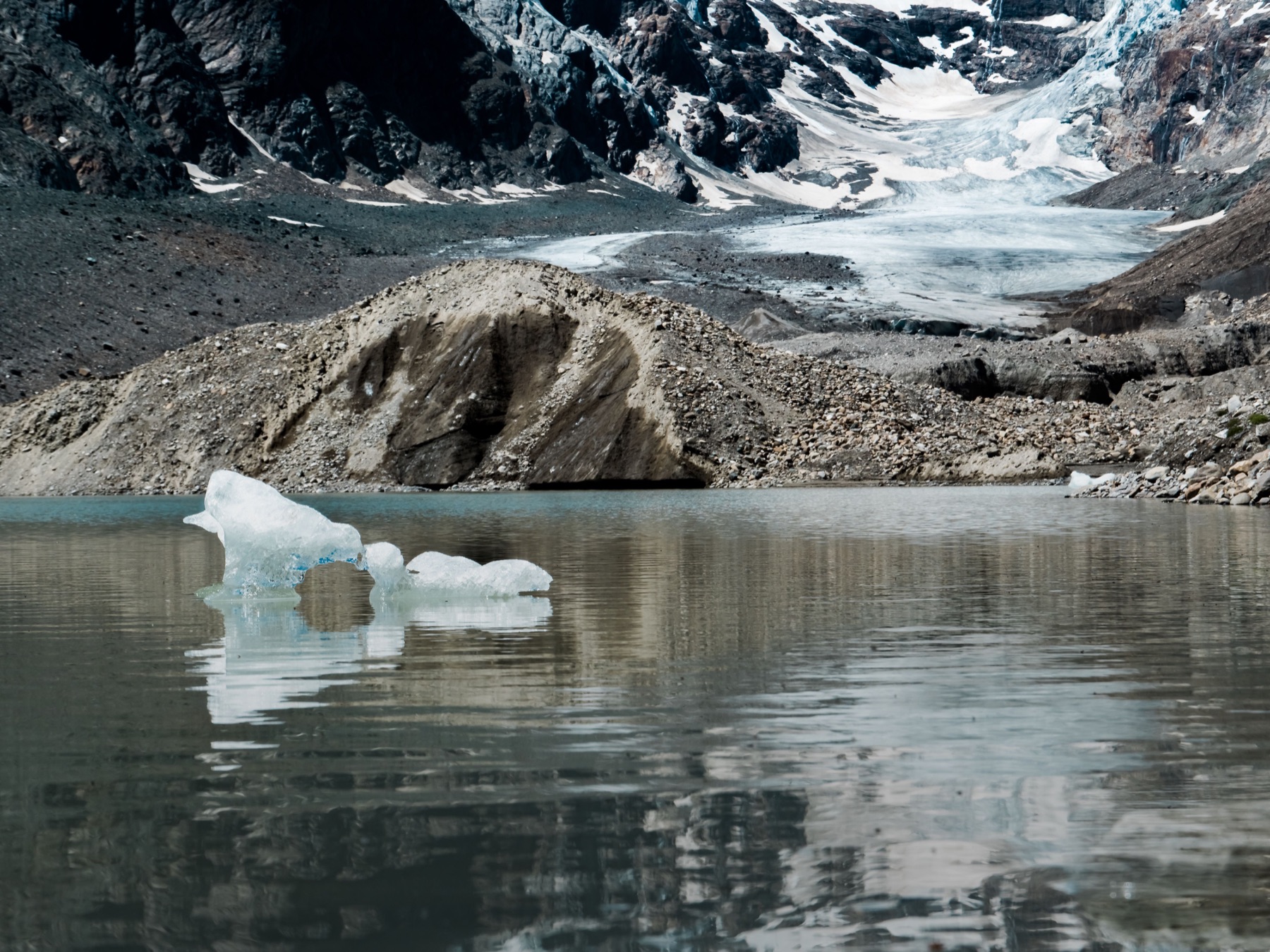 A floating piece of ice reflected in a lake below a mountain glacier